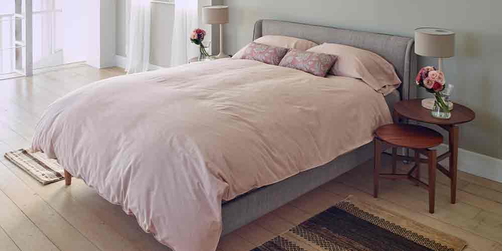 ベッドサイドテーブルのイメージ画像　ライトグレー布ベッドフレーム・淡いピンク色寝装品